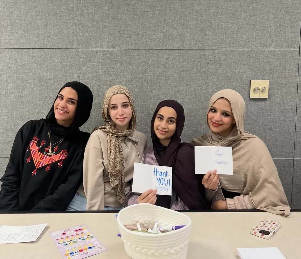 Four members at a card-making activity holding up handwritten “Thank you” and “Happy Holidays” cards.