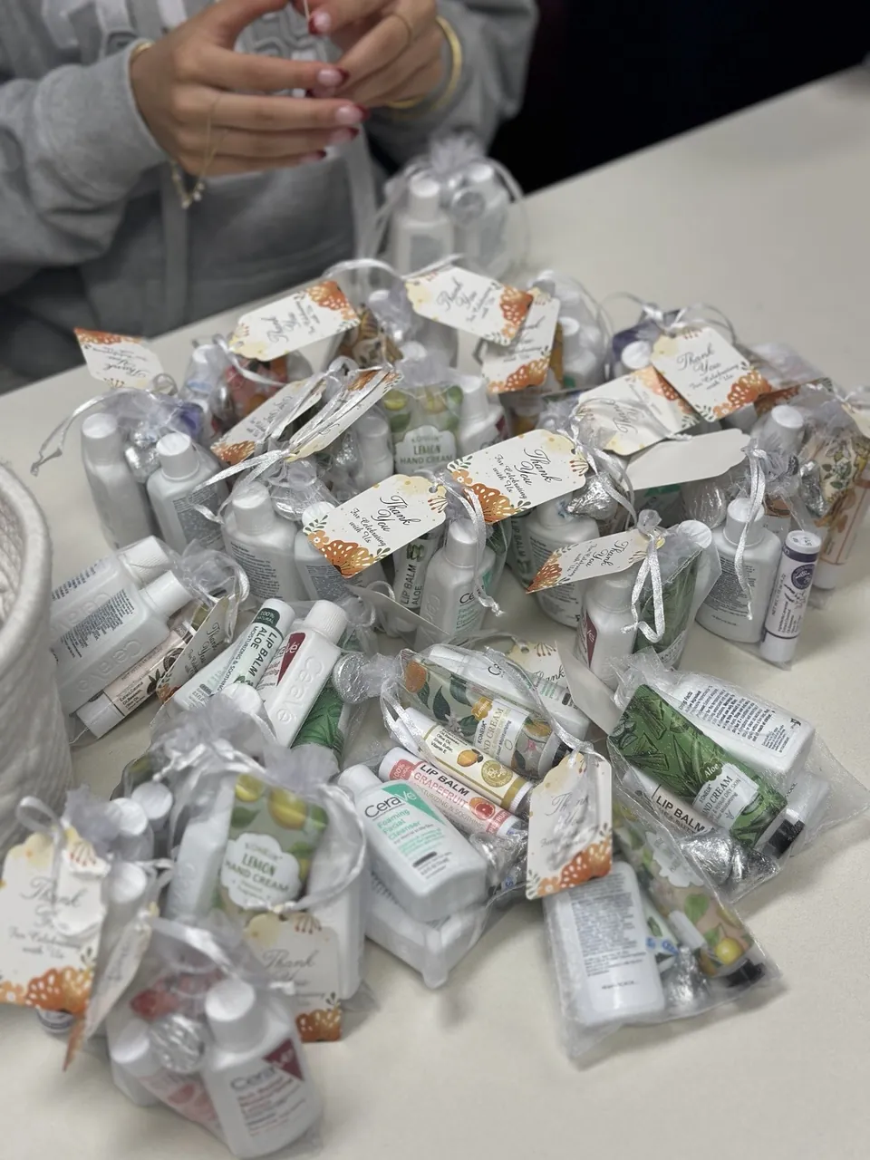 A table covered in finished care kits with hand cream, lip balm, and toiletries, each tied with a thank-you tag.