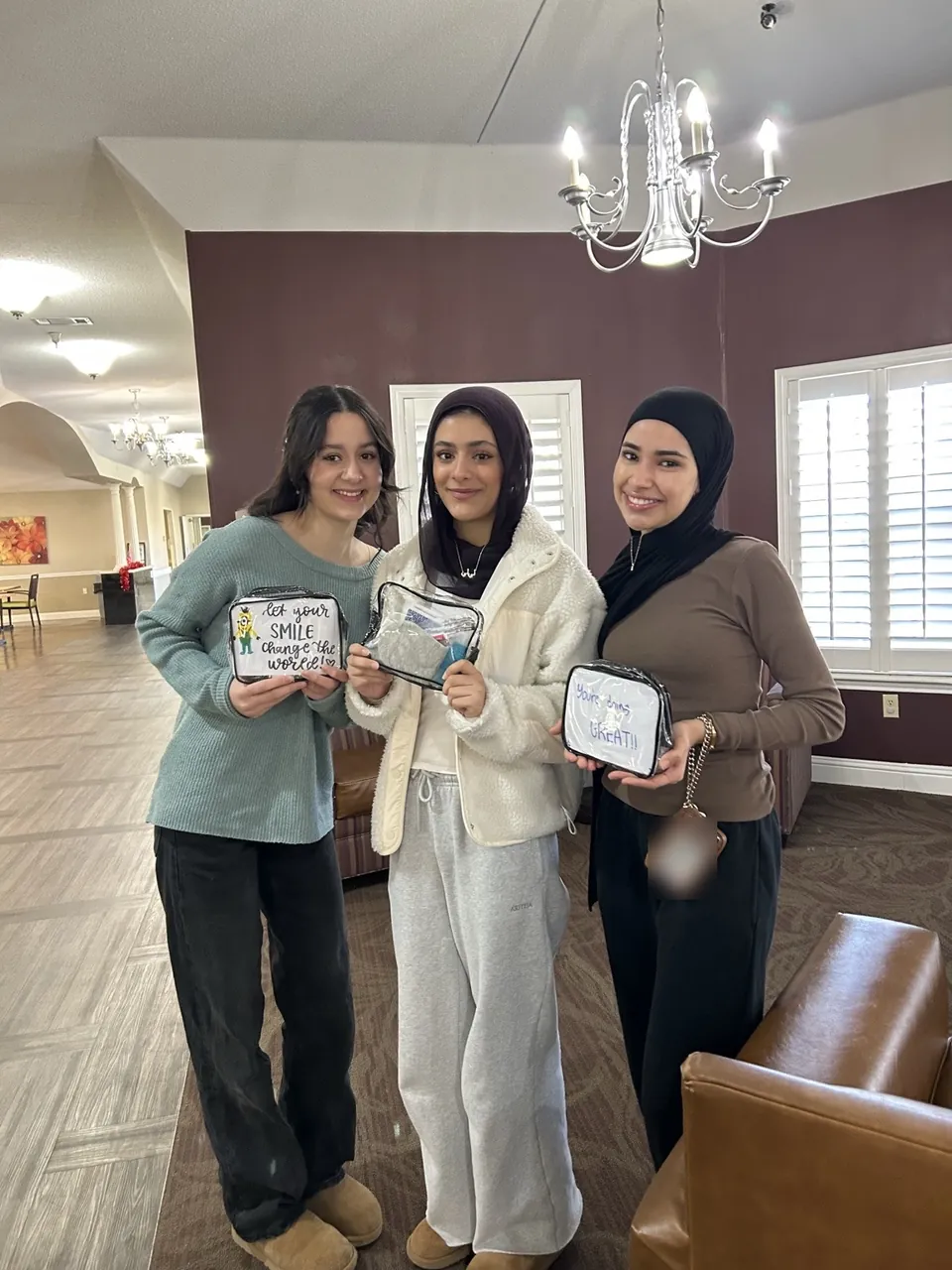 Three members at a nursing home holding clear pouches decorated with handwritten encouraging messages.