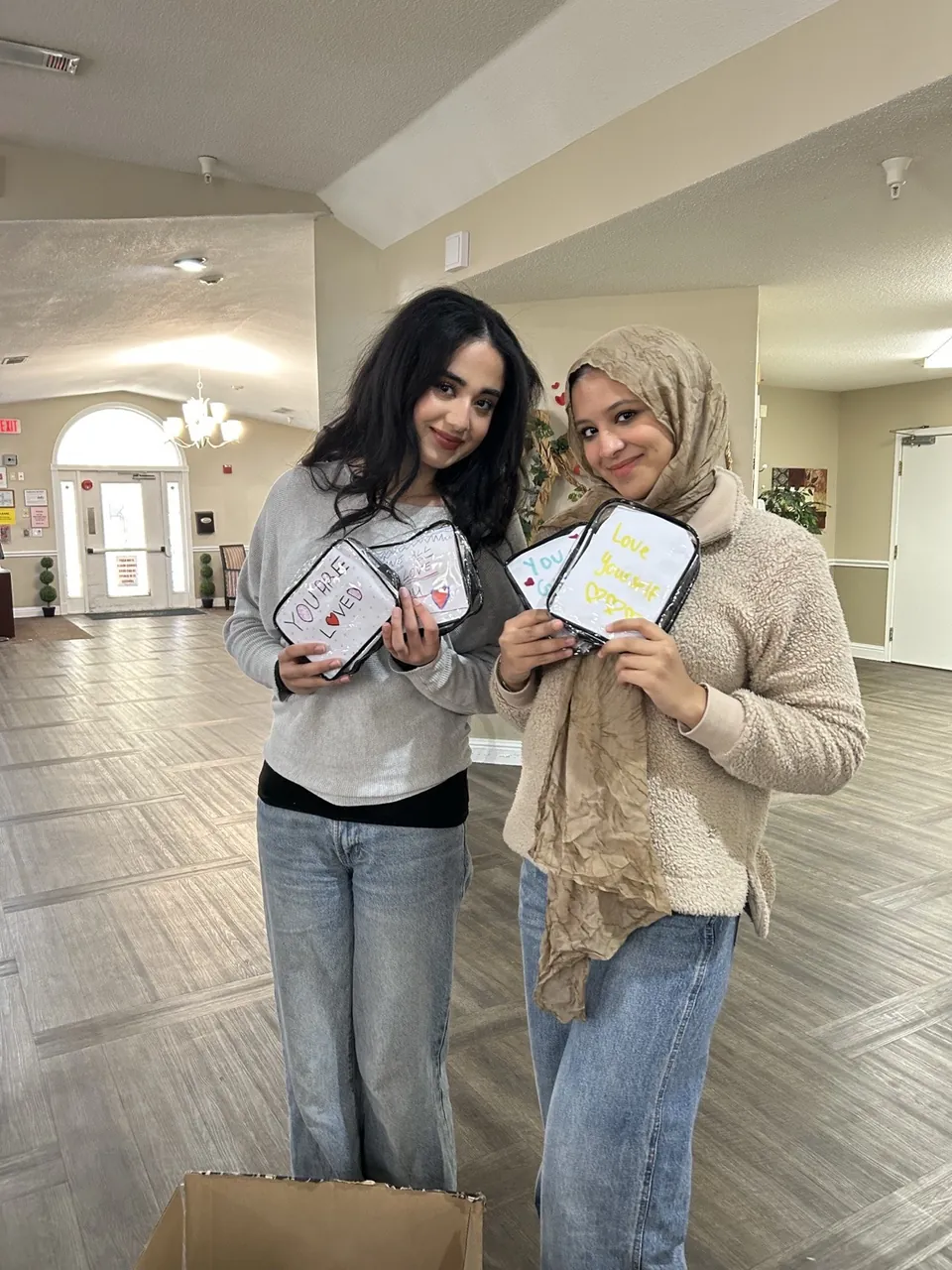 Two members at a nursing home holding pouches decorated with the messages “You are loved” and “Love yourself.”