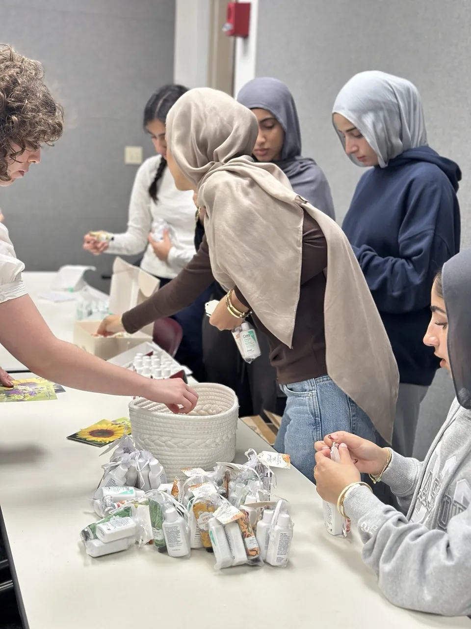 Students gathered around a table, filling care kits with hand cream and toiletries at a One Good Cookie meeting.